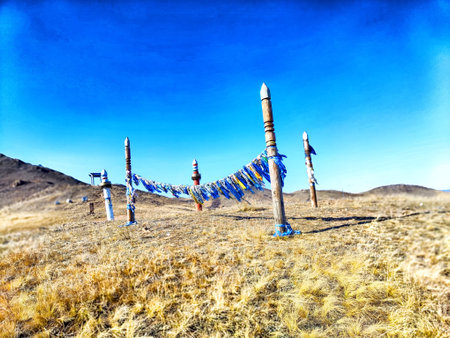 Vibrant prayer flags hang between wooden poles atop a mountain, gently swaying in the breeze against a bright blue sky.の写真素材