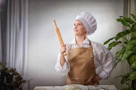 Elderly woman playfully posing with a rolling pin while cooking with flour in a cozy kitchen settingの写真素材