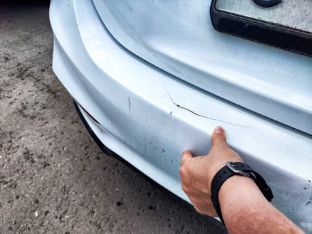 A person is seen pointing at a noticeable scratch on a silver colored cars exterior, drawing attention to the damaged areaの写真素材