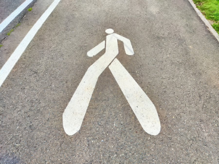A playful pedestrian symbol is painted on a path, featuring exaggerated legs in a park under clear blue skies.の写真素材