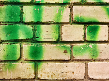 A weathered brick wall displays a unique texture with green and white colors, providing a versatile backdrop for text and design elements.の写真素材
