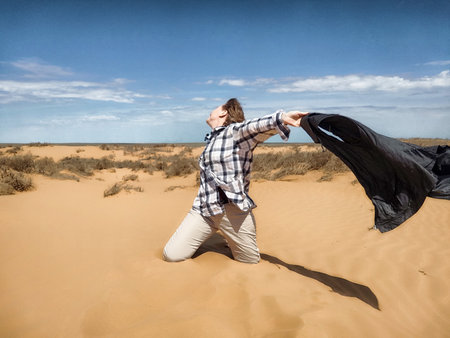 A middle-aged woman celebrates among the sand dunes, raising her arms against the clear sky, embodying freedom and joy.の写真素材