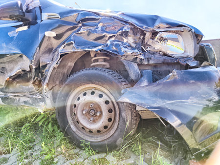 A black car shows significant damage to the front left side, parked near contemporary buildings in a sunny outdoor areaの写真素材