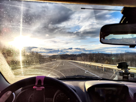 Car salon, windshield, hand of woman on steering wheel and landscape with sun in sunset. View from seat of driver on nature, Road in eveningの写真素材