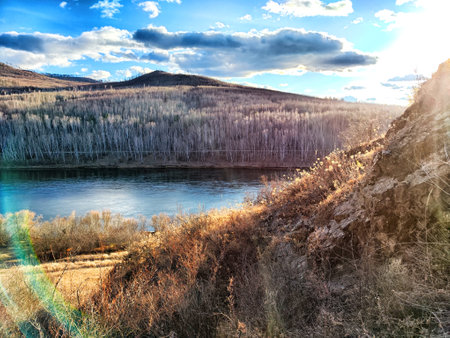 A tranquil river flows past vibrant trees under a colorful sky at dusk.