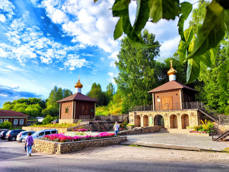 Two charming wooden chapels stand amidst vibrant flowers, with a clear blue sky and greenery in the background creating a peaceful atmosphere.の写真素材