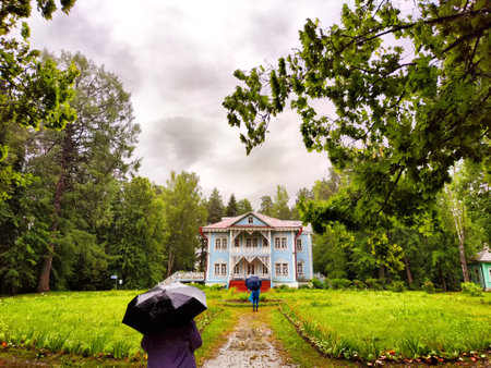 Visitors stroll towards a charming blue house amidst verdant grass and trees on a rainy day, highlighting nature's beauty.の写真素材