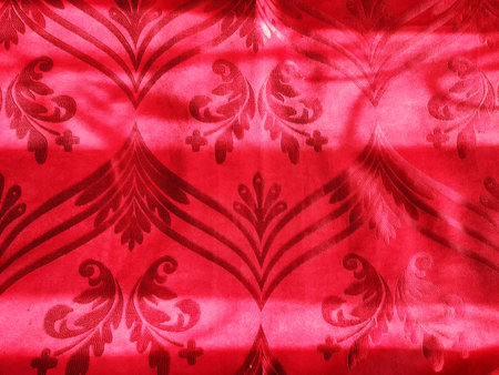 Rich red textile displays detailed floral patterns enhanced by subtle shadows, creating an inviting...