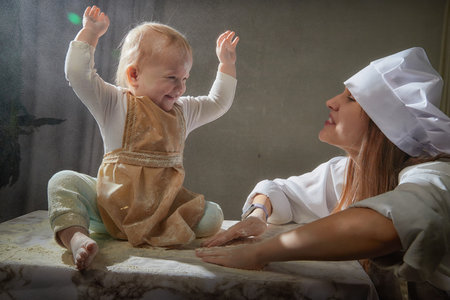 Mother and daughter in aprons joyfully playing with flour during a fun kitchen-themed photo shoot at homeの写真素材