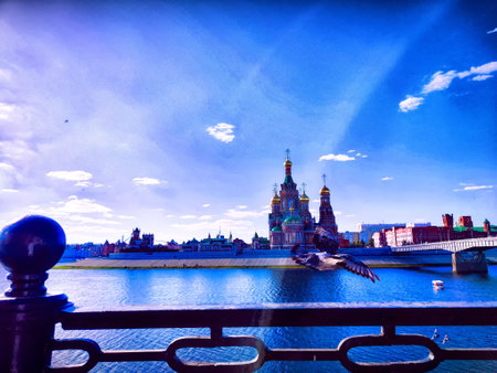 The iconic Church of the Savior on Spilled Blood towers against the blue sky as a bird takes flight over the river in St. Petersburg.の写真素材