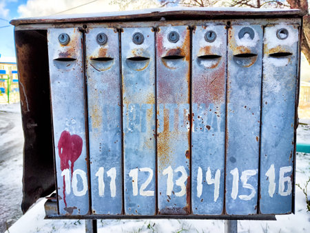 A weathered mailbox features numbered compartments and playful faces painted on the front, surrounded by a snowy landscape.の写真素材
