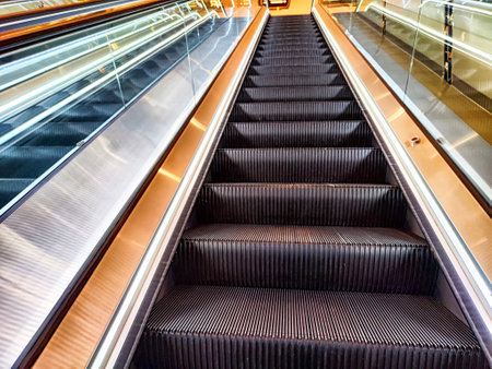 A sleek escalator ascends through a bustling shopping mall, surrounded by bright lighting and polished surfaces creating a vibrant atmosphere.の写真素材