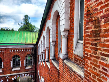 The red brick walls gracefully frame arches and columns, leading into a peaceful courtyard surrounded by trees under a cloudy sky.の写真素材