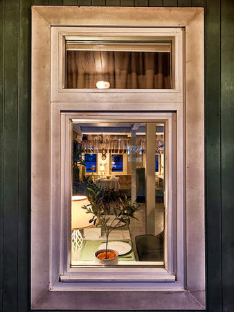 A view of a beautifully arranged interior with warm lighting and a small plant seen through the window during twilight.の写真素材