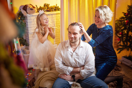 Family enjoys festive moments by the Christmas tree while preparing for New Year celebrations with joy and laughterの写真素材