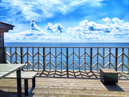 A beautiful wooden deck overlooks the sparkling ocean, with clear blue skies and soft clouds enhancing the tranquil atmosphere.の写真素材