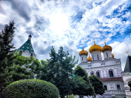 A beautiful garden features lush greenery and historic architecture with golden domes under a moody,...