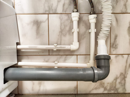 A close-up view of interconnected PVC and metal pipes beneath a sink in a renovated bathroom settingの写真素材