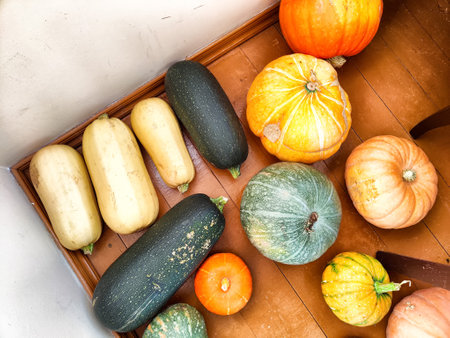 A variety of pumpkins and squash in different colors and shapes arranged on a wooden surface,...