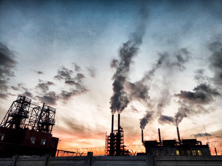 Thick, dark smoke rises from various industrial pipes against a vibrant sunset, illustrating the ongoing issue of air pollution in urban areas.の写真素材
