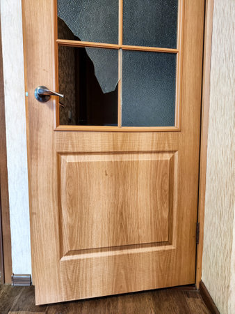 The wooden door displays a cracked glass panel, indicating damage in a well-lit interior space.の写真素材
