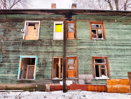 The old house stands neglected with weathered wood and broken windows, surrounded by snow in a...