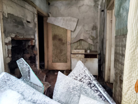 Fragmented glass from a broken window frames a neglected room, exposing crumbling walls and dusty kitchen cabinets in disrepair.の写真素材