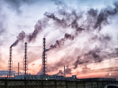 Dark smoke escapes from tall industrial pipes as daylight fades, creating an unsettling contrast...