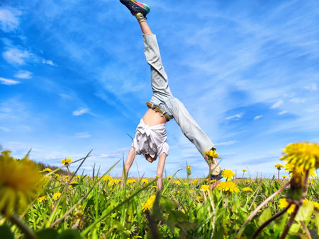 A person performs a handstand on a sunny day among blooming dandelions in a vibrant green fieldの写真素材