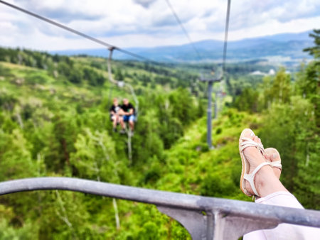 Travelers ride an open cable car above green valleys, taking in the stunning mountain scenery on a beautiful day.の写真素材