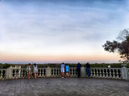 Groups of individuals gather on a balcony, admiring the beautiful sunset over a vast natural landscape.の写真素材