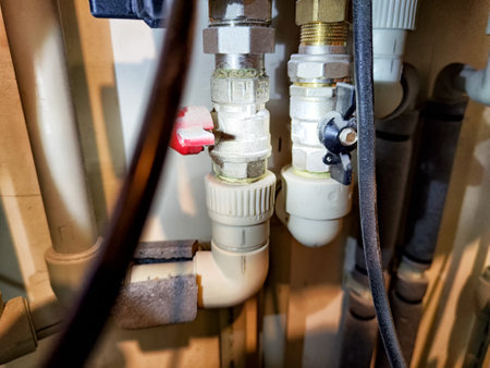 Plumbing pipes and valves are seen in a basement, showcasing maintenance activities with tools and equipment nearby.の写真素材