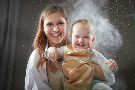 Mother and daughter in aprons joyfully playing with flour during a fun kitchen-themed photo shoot at...