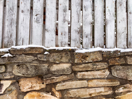 Weathered wooden fence top and uneven stone wall are dusted with fresh snow, creating a rustic winter atmosphere perfect for design ideas.の写真素材