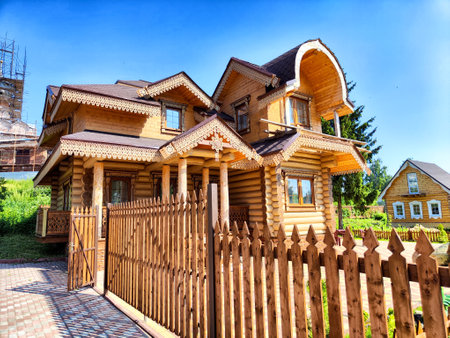 A beautifully crafted wooden house showcases unique architecture surrounded by lush greenery under a clear blue sky.の写真素材