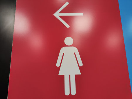 A clear directional sign showing a female figure with an arrow directing left, placed prominently in a restroom area.の写真素材