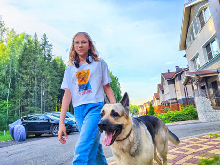 Young girl walks a German Shepherd dog along a suburban street surrounded by trees in the afternoon lightの写真素材