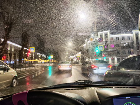 Drivers maneuver through a busy city street at night as colorful lights reflect on wet pavement, creating a lively urban scene.の写真素材