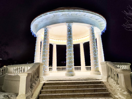 Illuminated gazebo with columns shines brightly in a snowy park during winter night, creating a serene and magical atmosphere.の写真素材