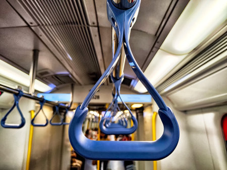 Close-up view of a blue handrail in a subway train with commuters in the background, highlighting...