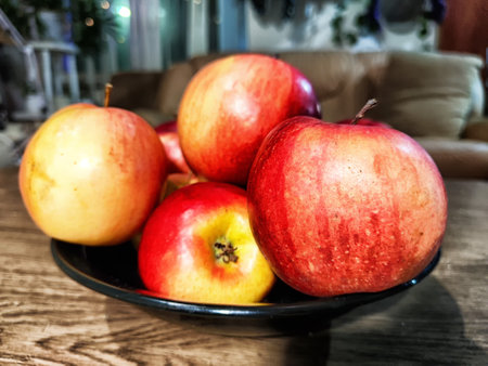 A bowl filled with assorted apples, featuring red and yellow varieties, sits on a wooden table in a...