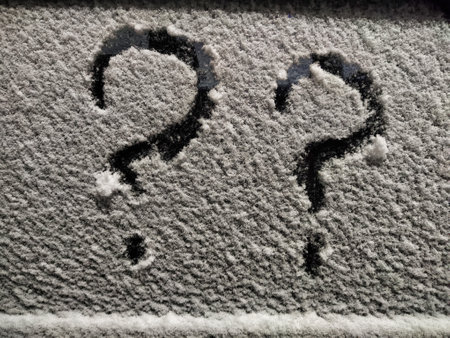 Question marks formed by snow on a surface symbolize hesitation and doubt in business strategies during winter.の写真素材