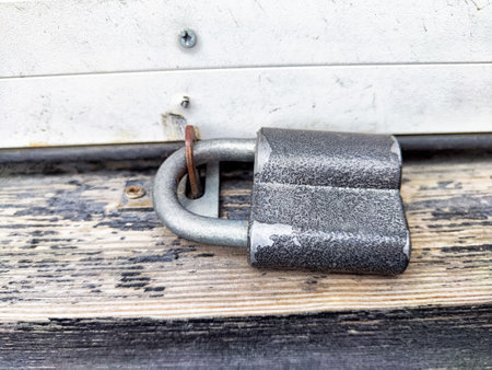 An old padlock lies on a rough wooden surface next to a building, indicating possible security or...