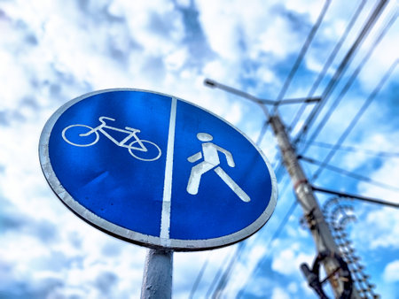Sign indicating bicycle and pedestrian use on a shared pathway under a bright blue sky with scattered clouds.の写真素材