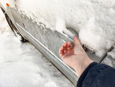 A hand reaches for a snow-covered car door handle, showing the challenges of winter driving.の写真素材