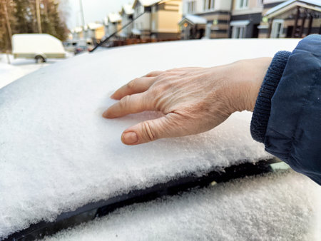 Driver inspects the icy layer on the car while standing in a snow-covered residential area during winter.の写真素材