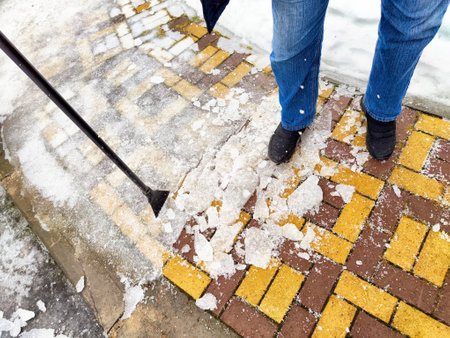 Person clearing snow and ice from a brick and stone walkway in a residential neighborhood during winter.の写真素材