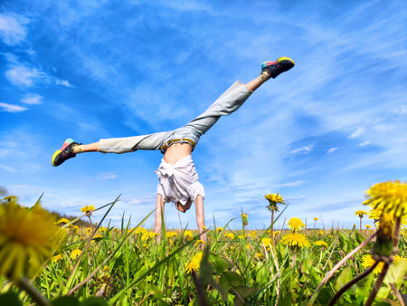 A person performs a handstand in a field of dandelions under a blue sky on a sunny dayの写真素材