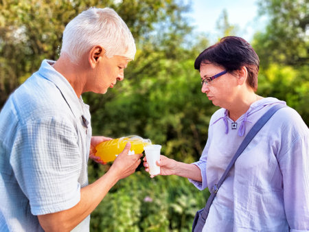 Elderly couple enjoying refreshing beverages outdoors at a sunny garden gatheringの写真素材