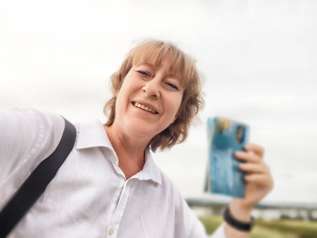 Middle-aged woman takes a joyful selfie while exploring a beautiful landscape on her travel excursion.の写真素材